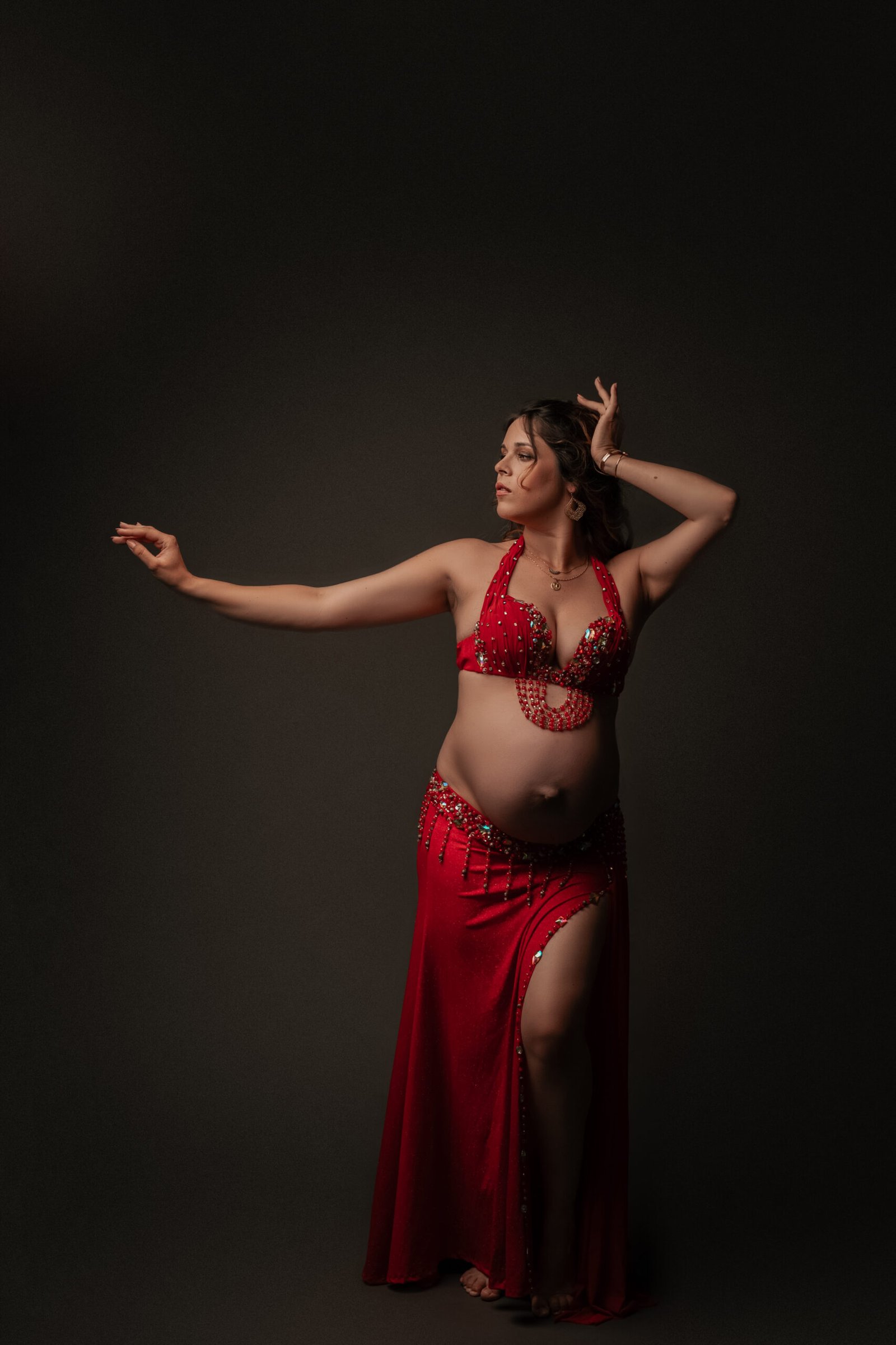 Alina enceinte en costume de danse orientale en studio, capturée en mouvement, illustrant la danse prénatale, la fluidité des gestes et l'expression corporelle douce et maternelle.